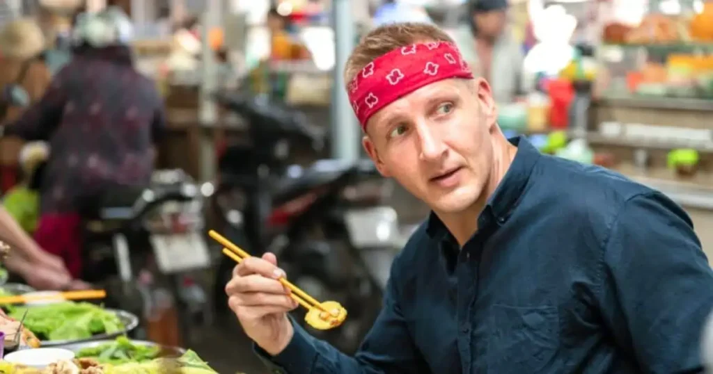 A man, Will Sonbuchner, dons a bandana and uses chopsticks, reflecting his distinctive approach to dining and culture.